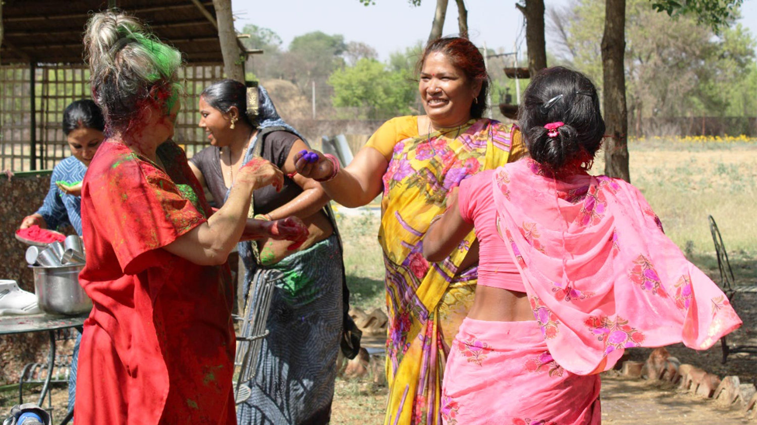 Group of women wearing saris and covering each other in colourful dyes to celebrate Holi.