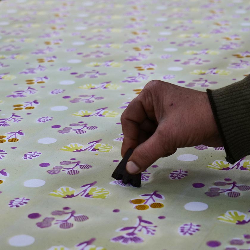 Hand holding a very small wooden block and printing a floral design.