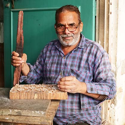 Carver holding a chisel and a nail with a big wooden block.