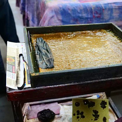 Detail of a wooden tray full of yellow dye ready for printing.