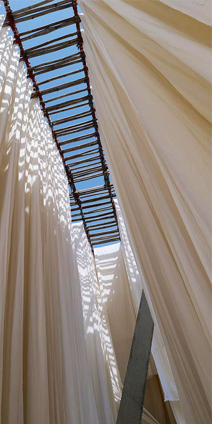 Long pieces of white fabric hanging on a bamboo structure to dry.
