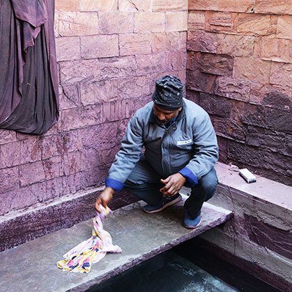 Man hitting a piece of freshly dyed cloth onto stone to remove excess water.