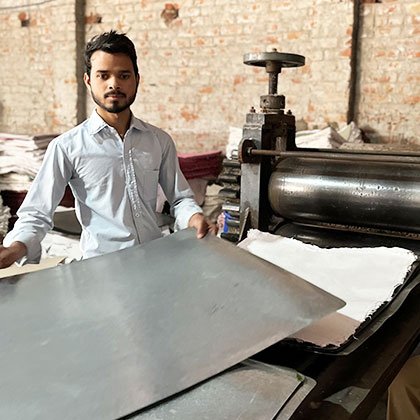 Young man using a machine to press sheets of handmade paper.