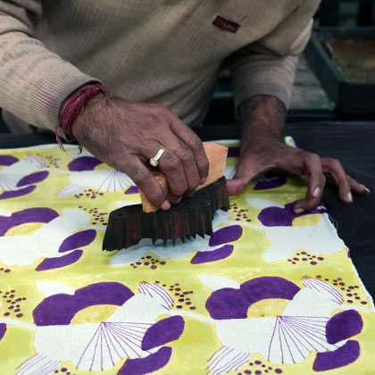 Detail of hand holding a wood block to print a section on a flower design.