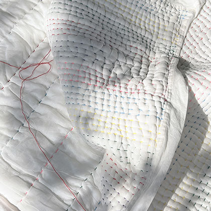 Close up of colourful running kantha stitching on white fabric.