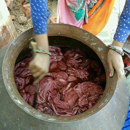 Detail of female hands stirring natural dyes inside a metal pot.