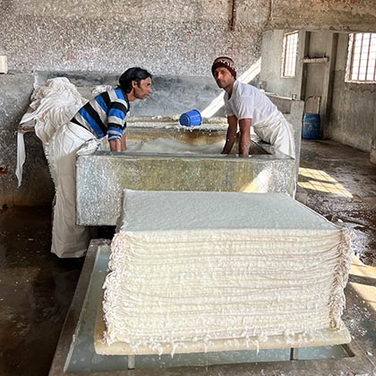 Two men with their hands inside a stone sink mixing water and paper pulp.