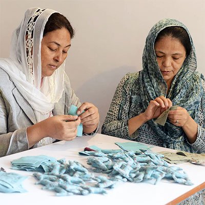 Two women hand stitching rag dolls clothes.