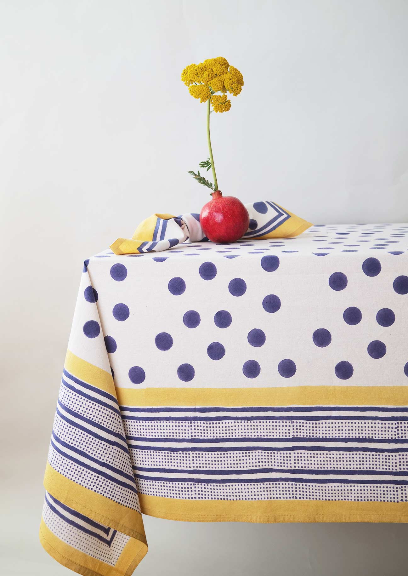 Table setting with co-ordinating tablecloth and napkin in a block printed navy spot on a white fabric base.
