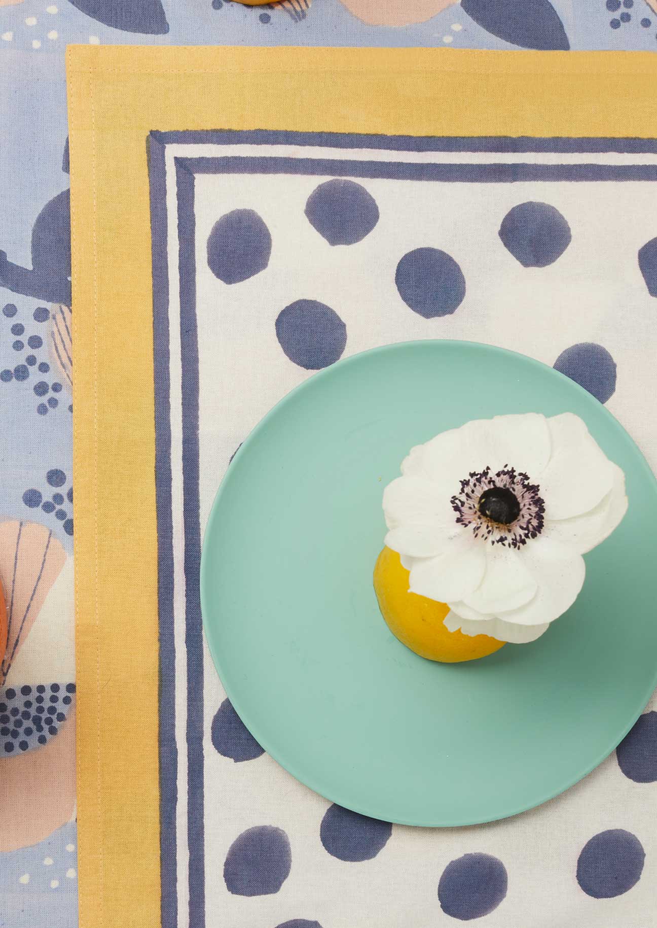 Navy spot block printed tablemat with yellow border and navy stripe edge detail layed over a blue floral tablecloth.