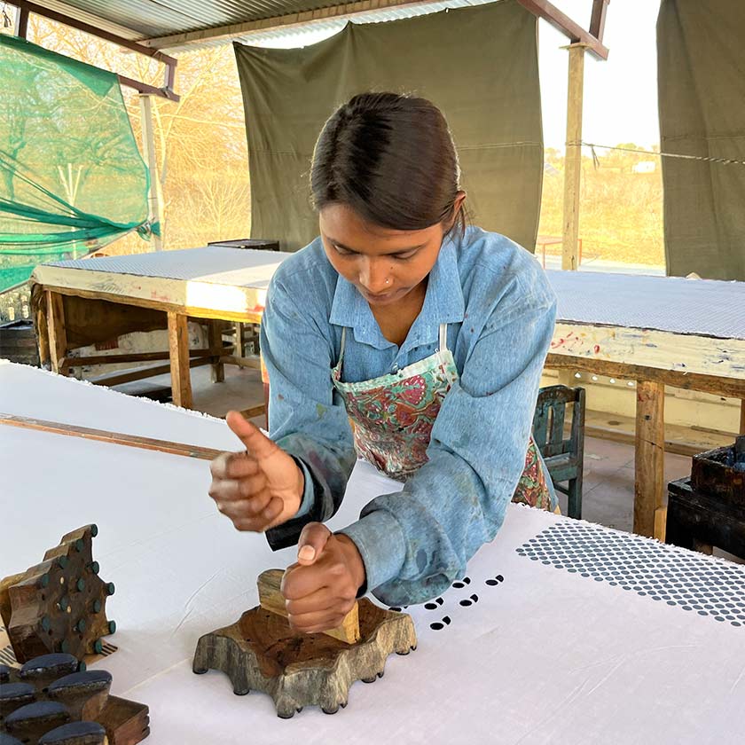 Girl using a wooden block and printing a simple design onto white fabric.