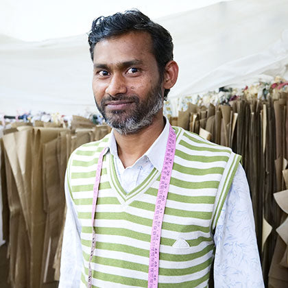Master tailor with measuring tape around his neck smiling at the camera.