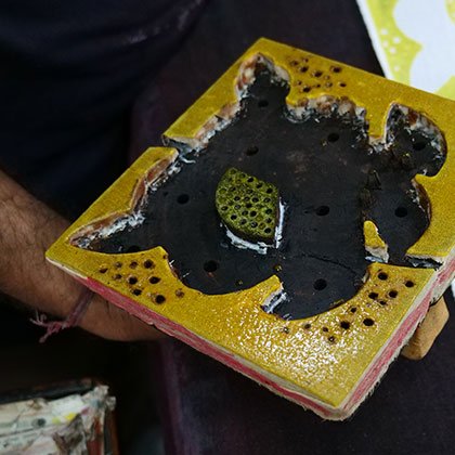 Floral design cut onto a square wooden block after being dipped in yellow dye.