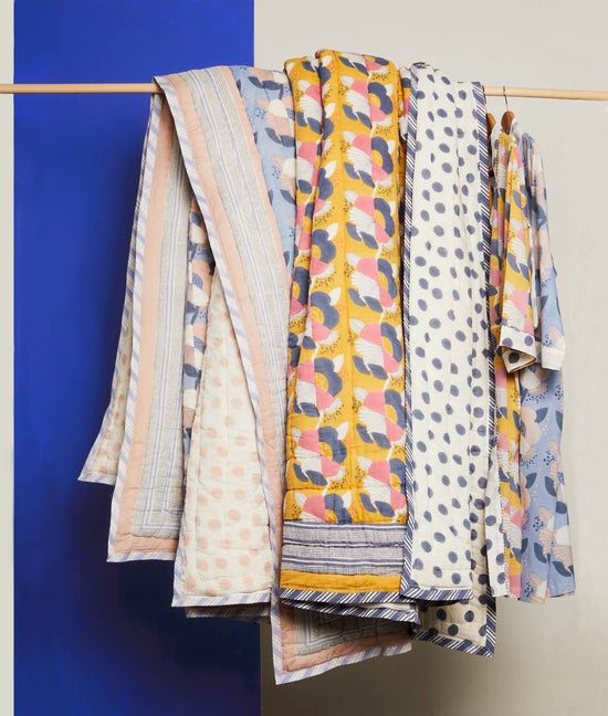 Collection of block printed floral quilts and robes hangign on a wooden pole.
