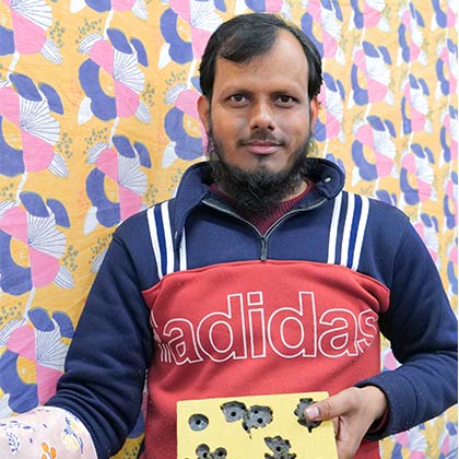Artisan holding a wooden block and showing the printed fabric created.