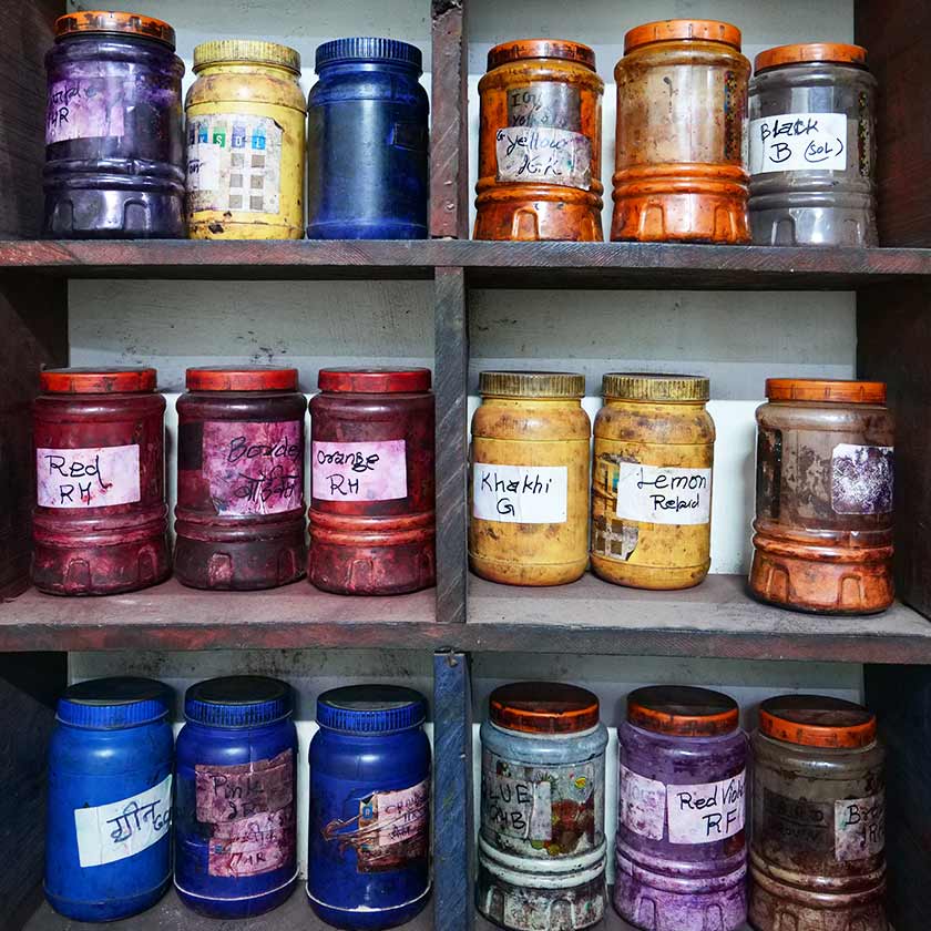 Plastic jars full of powder dyes on shelves.