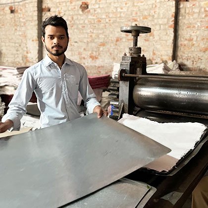 Young man using a machine to press sheets of handmade paper.