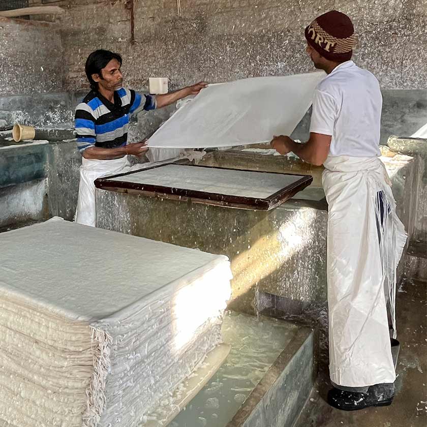 Two artisans holding a sheet of frehsly made khadi paper.