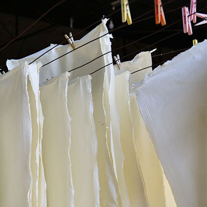 Sheets of handmade khadi paper hanging on clothes line to dry.