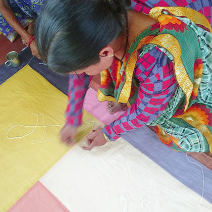 Artisan stitching a colourful patchwork quilt on the floor.