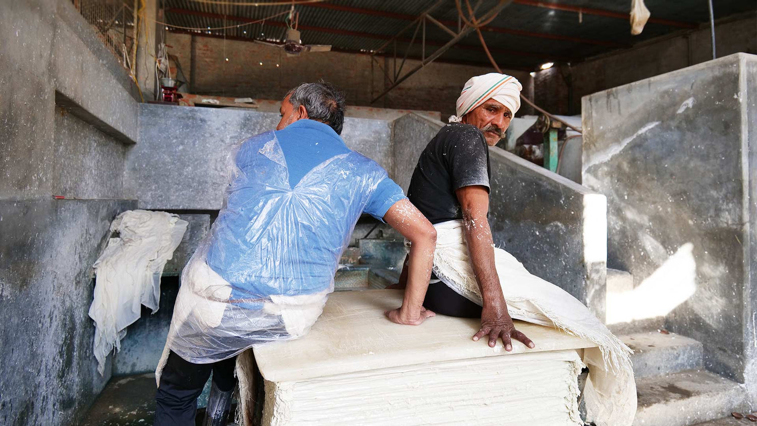 Two men sitting on a high pile of freshly made handmade paper to squeeze excess water out.