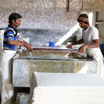 Men at handmade paper factory dipping a tray into a sink with water and water pulp mix.