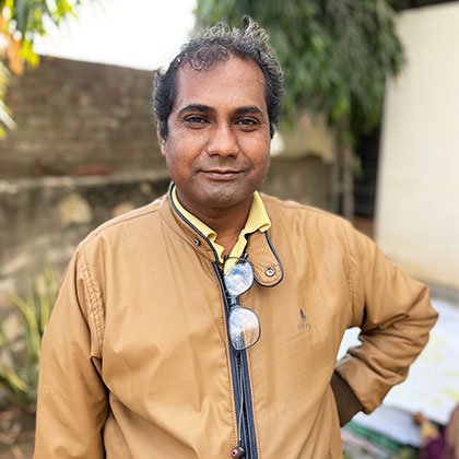 Indian man in ochre jacket smiling at the camera.