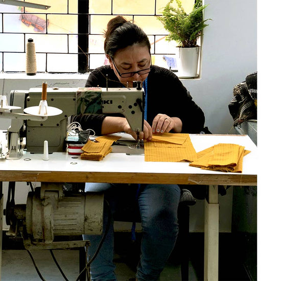 Woman sitting down using a sewing machine to stitch yellow fabric scraps.