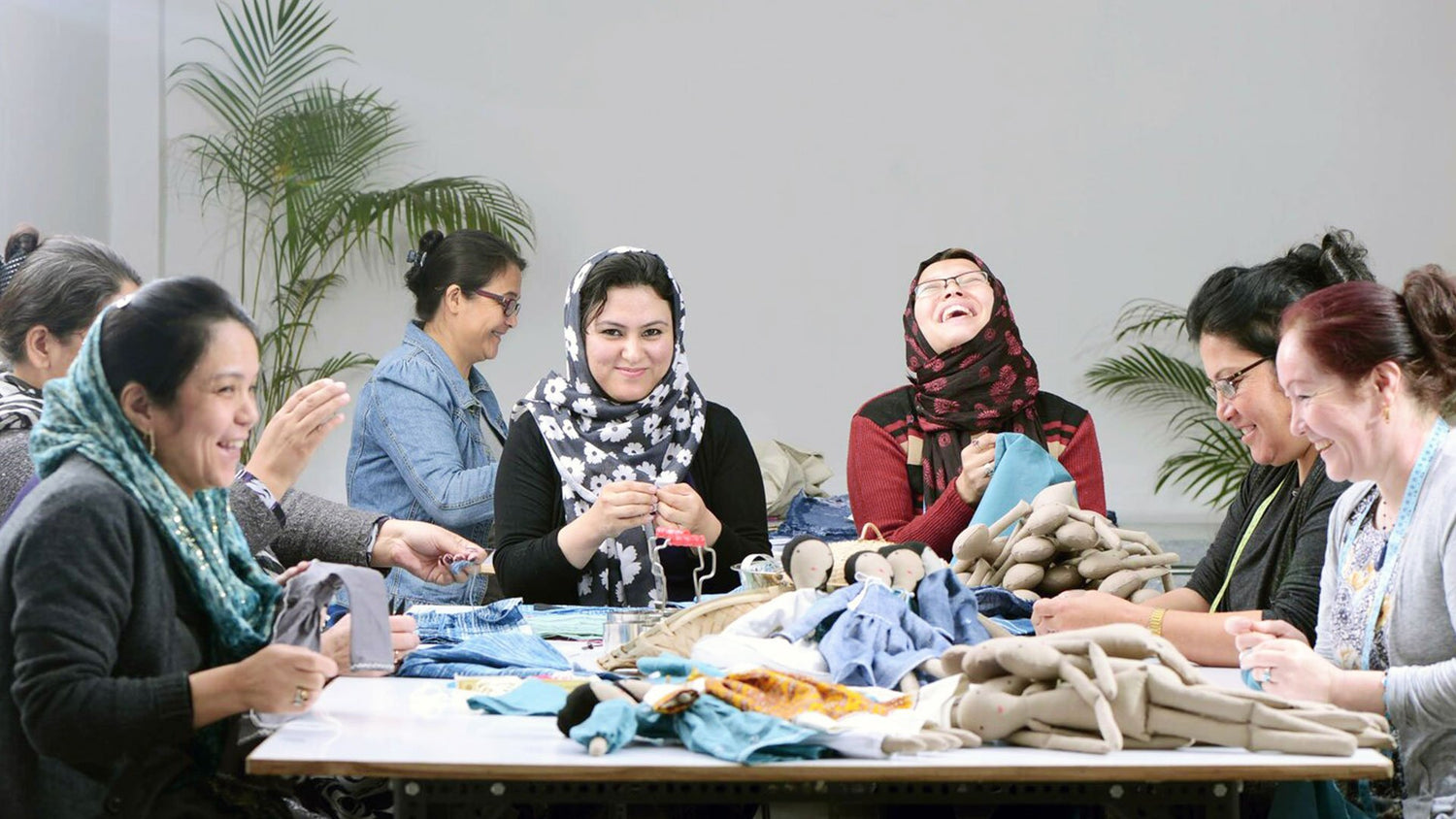 Group of Afghan refugees making rag dolls and smiling.