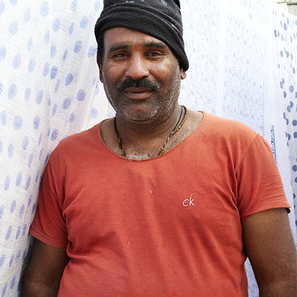 Headshot of smiling Indian man in front of block printed fabric.