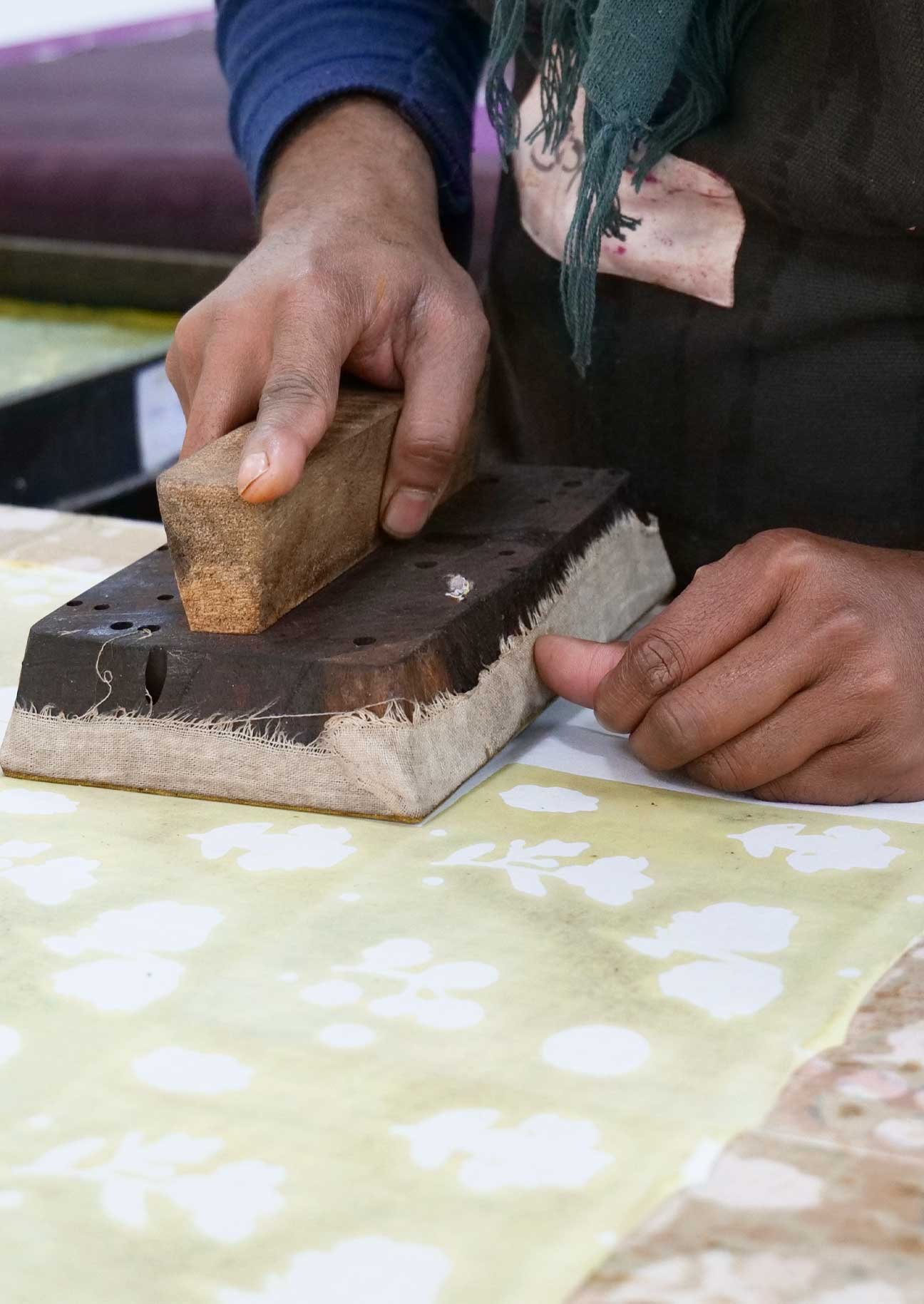Block print artisan using a wooden block to print a floral motiff onto cotton cloth