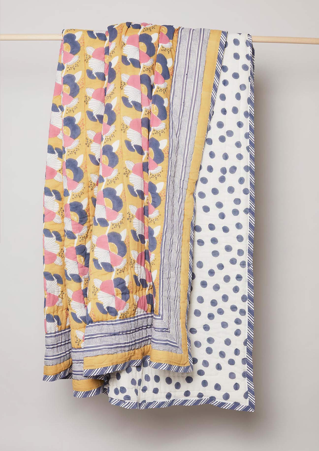 Yellow, blue and pink floral block printed quilt with stripe edge design and navy polka dot reverse.