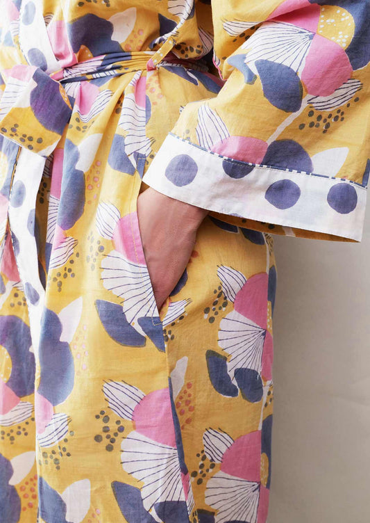Close up of ochre yellow robe which has been block printed and features a large scale floral print in navy, pink and white tones. 